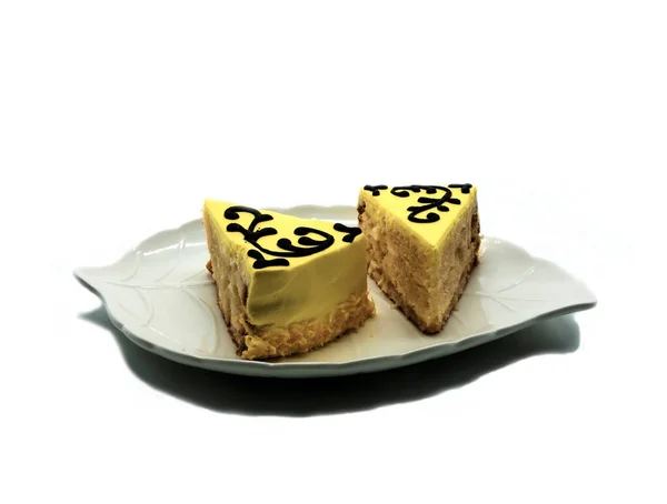 一块白色的叶子形的盘子上有两块蛋糕 蛋糕上涂有黄色的奶油 并装饰有巧克力釉料 在白色背景下被隔离 — 图库照片