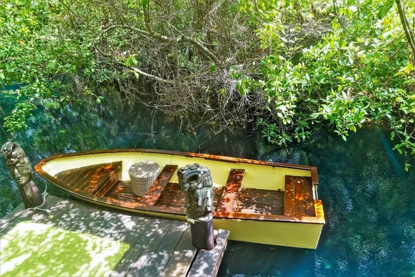 A yellow wooden boat is moored. The water in the river is turquoise. On the shore there are tropical thickets. Mexico.