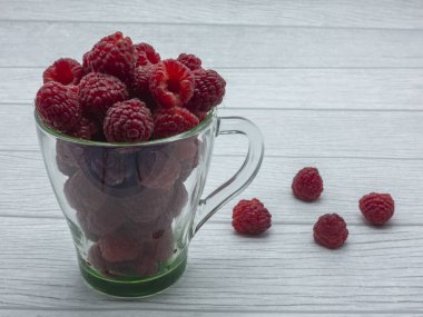 İçi ahududu dolu şeffaf cam bardak. Birkaç dut masanın üzerinde yan yana yatmaktadır. Beyaz arkaplan.