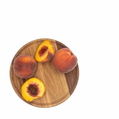 Yuvarlak tahta üzerinde taze şeftaliler. İki meyve tam, biri ikiye bölünmüş. Yarım daire şeklinde yatıyorlar. Yukarıdan bak. Beyaz arkaplan üzerinde izole edilmiş.