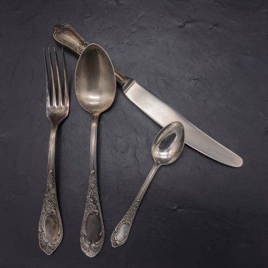Cupronickel 'dan bir çatal bıçak takımı: masa, çay kaşığı, çatal, bıçak. Her şey yirminci yüzyılın başında üretildi, 100 yıldan fazla bir süre önce, bir güherçile ile ile kaplıydı. Arka planda siyah taş var..