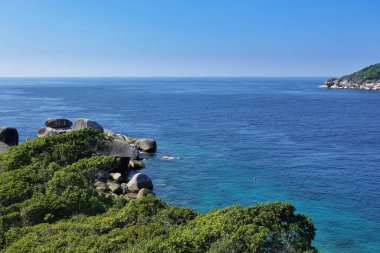 Yeşil bir tropikal adanın kıyısında büyük kayalar bulunur. Turkuaz deniz sakindir. Açık mavi gökyüzü, ufukta su var. Tayland. Phuket.