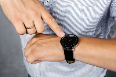 Gömlekli bir adam kol saatini işaret ediyor.