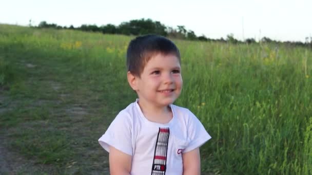 Au ralenti. Un petit garçon de 3 ans en T-shirt blanc rit. Enfance dans le champ dans la nature, bonheur. Un sourire pour les parents et la famille, pour maman et papa.