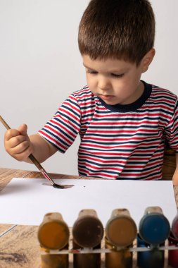 Çizgili renkli tişört giyen 2-3 yaşlarında küçük bir çocuk kağıda guasya resmi çiziyor. Çocuklar için eğlence ve eğlence, çocuk gelişimi, erken gelişim. Bebeklerin renkli çizimleri