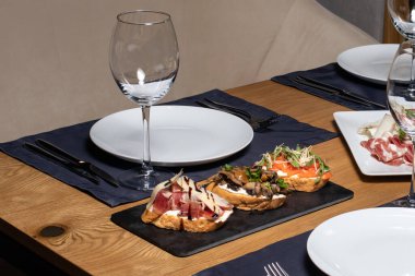 Restorandaki ahşap masada dilimlenmiş somun, mantar, somon ve etten oluşan üç bruschetta. Atıştırmalık ve sandviç.