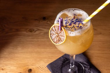 Büyük bardakta alkollü kokteyl, bir dilim portakal ve siyah arka plandaki ahşap bir masada bir tüp. Şampanya ve votkayla iç.