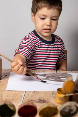 Çizgili parlak bir tişörtle 2-3 yaş arası küçük bir oğlan çocuğu gouache renklerini resmediyor. Renkli çizimler, çocukların yaratıcılığı..