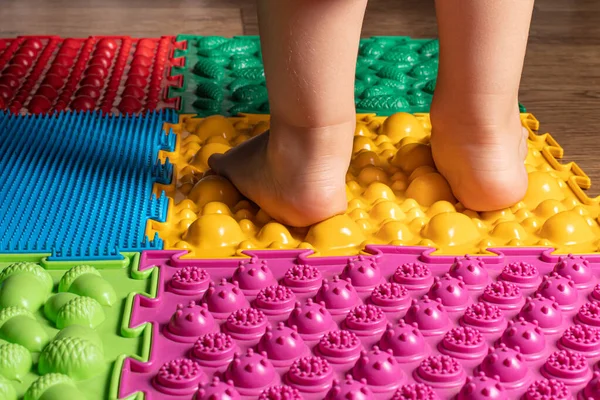 Egy kisgyerek lábai az ortopéd szőnyegen. Fényes felületek a gyalogláshoz és a láb megfelelő ívének kialakításához. Masszázs puzzle szőnyeg. — Stock Fotó