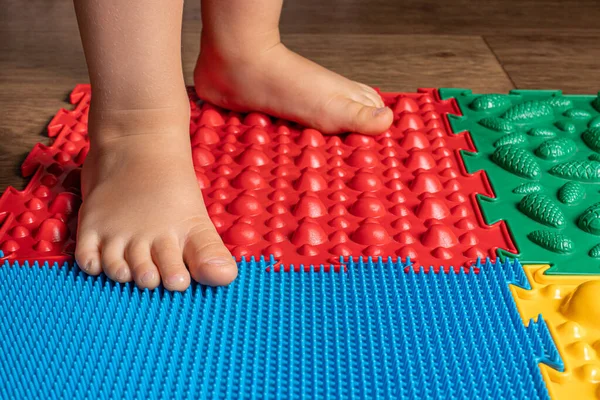 Las piernas de un niño pequeño en alfombras ortopédicas. Superficies brillantes para caminar y formar el arco correcto del pie. Masaje rompecabezas estera. — Foto de Stock