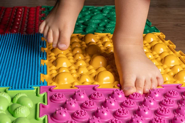 Le gambe di un bambino piccolo su stuoie ortopediche. Superfici luminose per camminare e formare l'arco corretto del piede. Massaggio puzzle mat. — Foto Stock