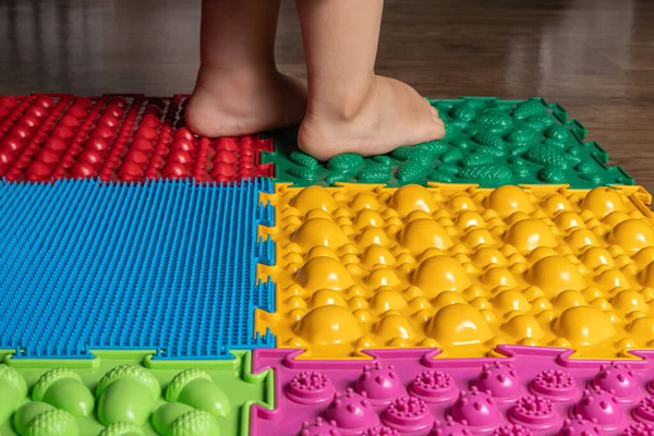 Egy kisgyerek lábai az ortopéd szőnyegen. Fényes felületek a gyalogláshoz és a láb megfelelő ívének kialakításához. Masszázs puzzle szőnyeg. — Stock Fotó