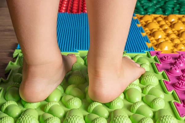 Las piernas de un niño pequeño en alfombras ortopédicas. Superficies brillantes para caminar y formar el arco correcto del pie. Masaje rompecabezas estera. —  Fotos de Stock