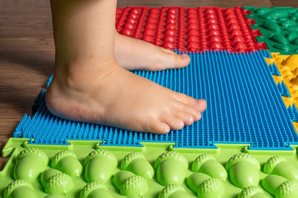 Las piernas de un niño pequeño en alfombras ortopédicas. Superficies brillantes para caminar y formar el arco correcto del pie. Masaje rompecabezas estera. — Foto de Stock