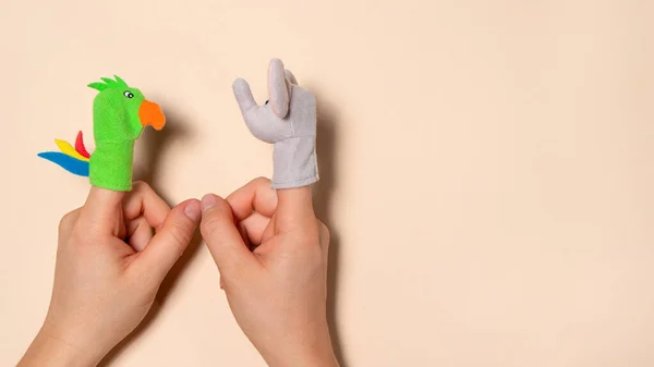 Fingers toys made of fabric on the hands on a beige background. Fingers Theatre. Two arm with toys animals elephant and parrot