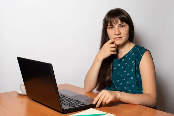 A brunette woman sits at a table in front of a laptop. Work from home. Online training. — Stock Photo, Image