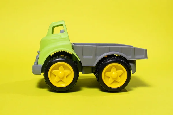 Toy truck car on a yellow background - construction equipment for children. Bright childrens plastic toys, dump truck childhood.