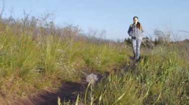 Mavi kot ceketli ve kot pantolonlu güzel bir kız doğada yeşil bir alanda dolup taşan şehirden uzakta yürüyor..