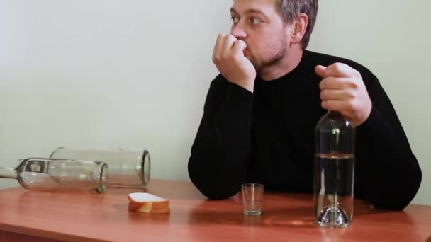 A man in alcoholic intoxication sits at a table and holds a bottle of alcoholic beverage. Vodka, delirium, dependence on alcohol. Social problems — Stock Footage Man Alcoholic Intoxication Sits Table Holds Bottle Alcoholic Beverage Vodka Royalty Free Stock Footage