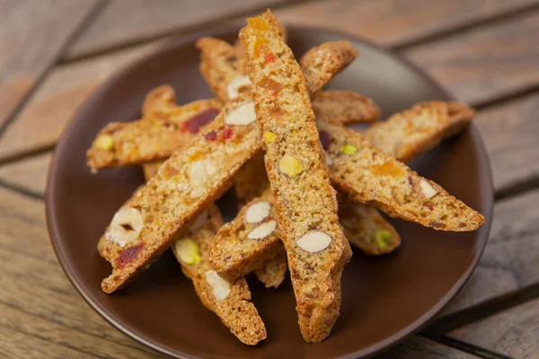 Ev yapımı bisküvi, fındıklı ve şekerli meyveli, kahverengi bir tabakta, ahşap bir masada.