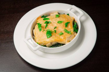 Peynir yastığının altında sebzeyle pişirilmiş somon balığı. Beyaz bir tabakta. Siyah sırtüstü