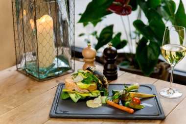 Izgara sebzeli siyah yengeç burger. Ve bir bardak beyaz şarap. Siyah bir tabakta. Kırsal bir ahşap masada