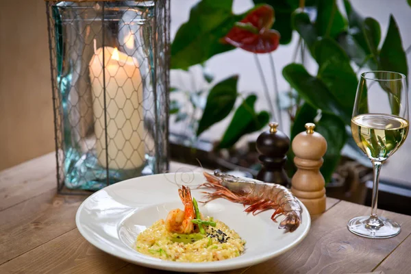 Karides, kuşkonmaz ve kaplan karidesli risotto. Beyaz bir tabakta. Ve bir bardak beyaz şarap. Kırsal bir ahşap masada