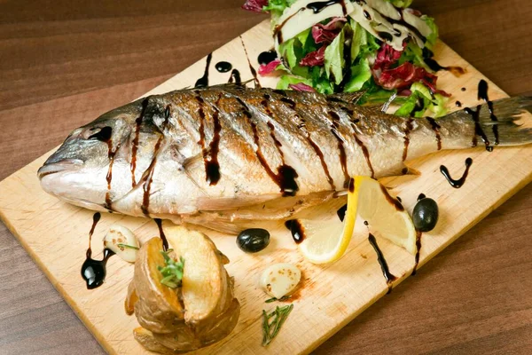Izgara levrek, kızarmış patates ve taze salata. Zeytin ve limonla Tahta tepside