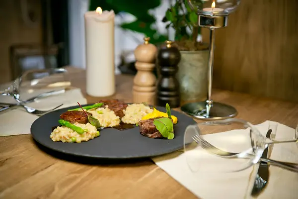Bulgur ve kuşkonmazlı sığır eti madalyonu. Siyah bir tabakta. Bir restoranın arka planına karşı.