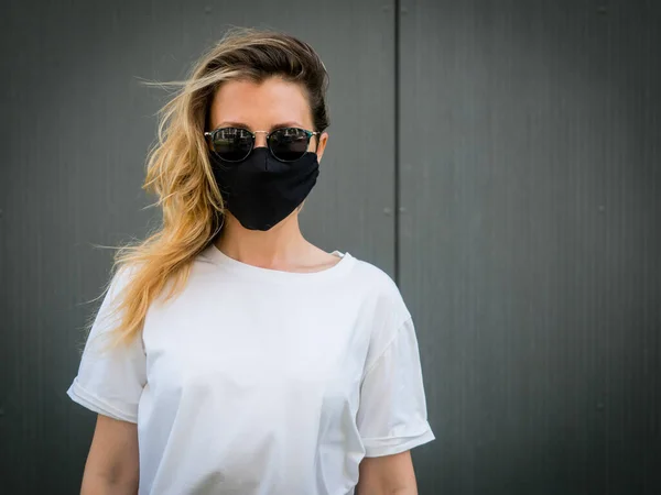 Siyah koruyucu maske takan bir kız. Gri bir arkaplanda. Koronavirüs salgını sırasında
