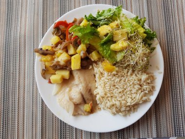 Pirinçli bir balık yemeği ve arka planda masa örtüsü olan ananaslı salata.