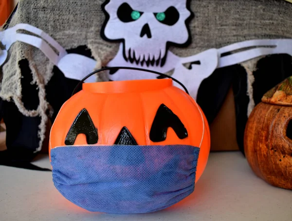Plastic pumpkin with a medical mask for halloween decoration, and a skeleton, covid