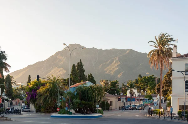 Marbella şehrinde yüksek kaktüslü dairesel bir kavşak, iki dar cadde yukarı çıkıyor ve Sierra Blanca dağı arka planda batan güneş tarafından aydınlatılıyor.