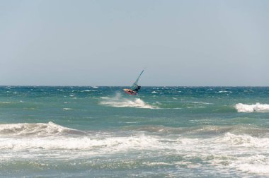 Bir rüzgar sörfçüsü Akdeniz 'in dalgalarında güneşli bir günde dalgalara atlar ve atlar..