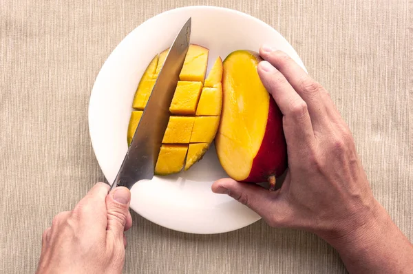 İki erkek eli tabakta bıçakla mango kesiyor.