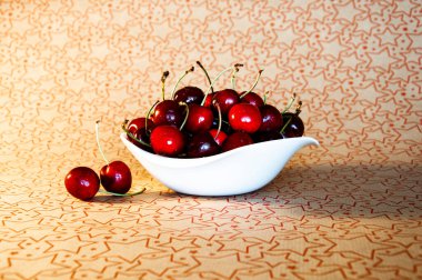 Farklı kiraz tonlarına sahip beyaz çay tabağı kırmızı çizgili bej bir yüzey üzerindedir.