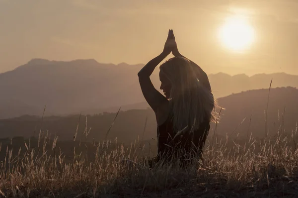 Bir kız, dağ tepeleri ve günbatımının arka planında Tarva 'nın kulakları arasında yoga yapıyor.