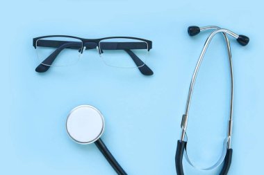 Mavi arka planda duran steteskop ve gözlük. Tıbbi ekipman konsepti.