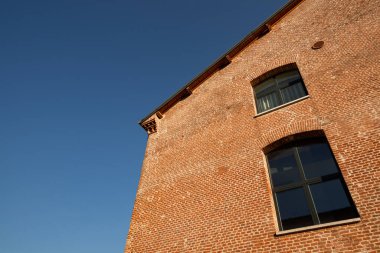 Kompozit tarzda yönlü bir binanın detayları. Büyük mavi cam yüzeyler ve tuğla duvarlar, fırçalanmış çelikten detaylar, bulutsuz öğleden sonra.