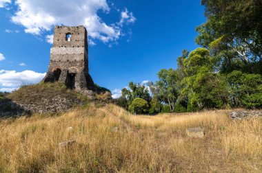 Cenaze anıtının heybetli yapısı Torre Selce Via Appia Antica, Roma, İtalya 'da tuğlada. Sarı bir çayırla çevrili güneş ve bulutlarla dolu bir yaz gününde çekilmiş..