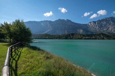 Cavedine Gölü Trentino. Turkuaz mavi suların manzarası, harika ahşap çitleri, zengin bitki örtüsü ve dağları var. Cavedine Gölü, İtalya 'nın Alto Adige kentinde bulunan küçük bir alp gölüdür.,