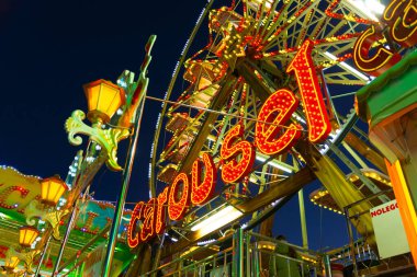 Atlıkarınca, arka planda dev dönme dolap akşam mavi gökyüzü. Lunaparkın dış tarafında renkli ışıklarla aydınlatılmış asılmış arabaların olduğu dev dikey dönen tekerleği olan bir lunaparkta.