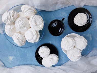 Bir kasede beyaz şekerlemeler ve siyah bir tabakta ve mavi desenli arka planda bir fincan çay. 