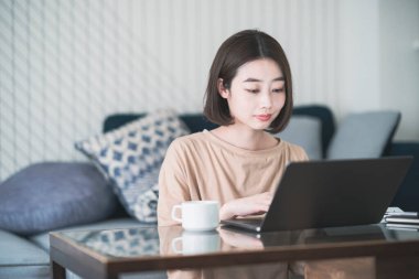 Evde dizüstü bilgisayarla uzaktan çalışan Asyalı genç bir kadın.