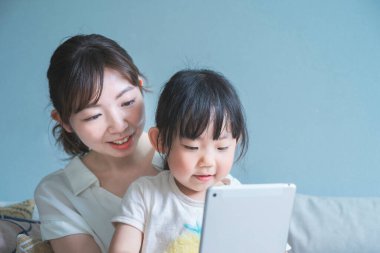 Anne ve kızı kanepede oturuyor ve tablet bir cihaz kullanıyorlar.