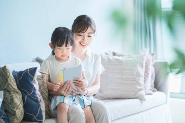 Anne ve kızı kanepede oturuyor ve tablet bir cihaz kullanıyorlar.