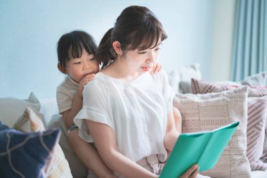 Anne ve kızı kanepede oturup resim kitabı okuyorlar.