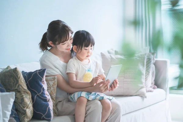 Anne ve kızı kanepede oturuyor ve tablet bir cihaz kullanıyorlar.