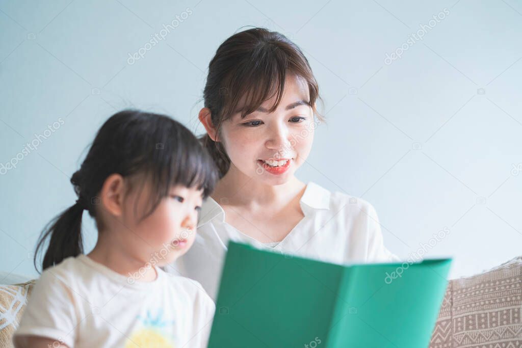 Mother and daughter sitting on the sofa and reading a picture book