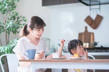 Asyalı anne ve kızı evdeki yemek masasında pasta yiyorlar.